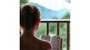 Persona leyendo un libro en un balcón tranquilo con vista a la naturaleza.